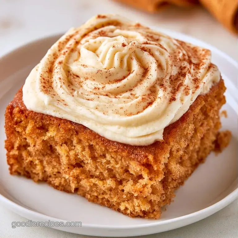 Elegant slice of golden cake on a white plate, topped with velvety frosting and a dusting of warm cinnamon powder.